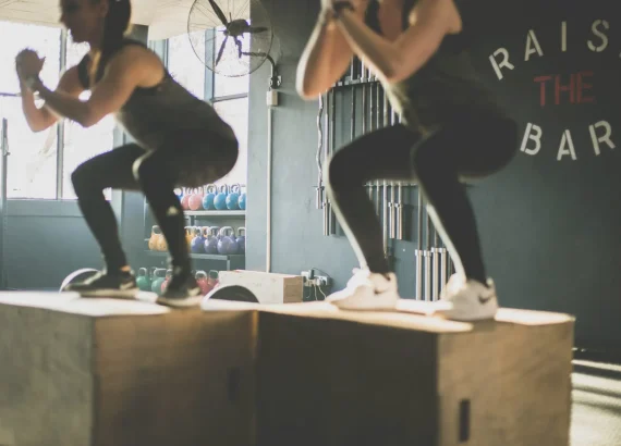 Two people performing box jumps in a gym as part of their high-intensity interval training routine.