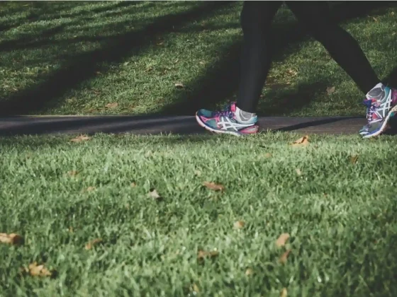 a person walking on a grassy path with fallen leaves