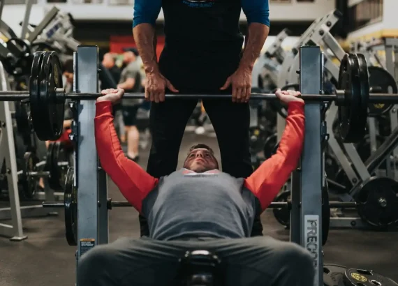 A man performing a incline bench exercie at a gym while a trainer supervises, illustrating a strength training exercise