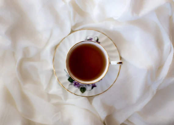 A cup of tea in a delicate, floral-patterned teacup, set on a soft white fabric, a soothing alternative to coffee.