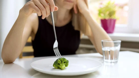 Woman eating broccoli as part of calorie restriction