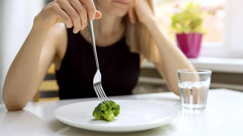Woman eating broccoli as part of calorie restriction