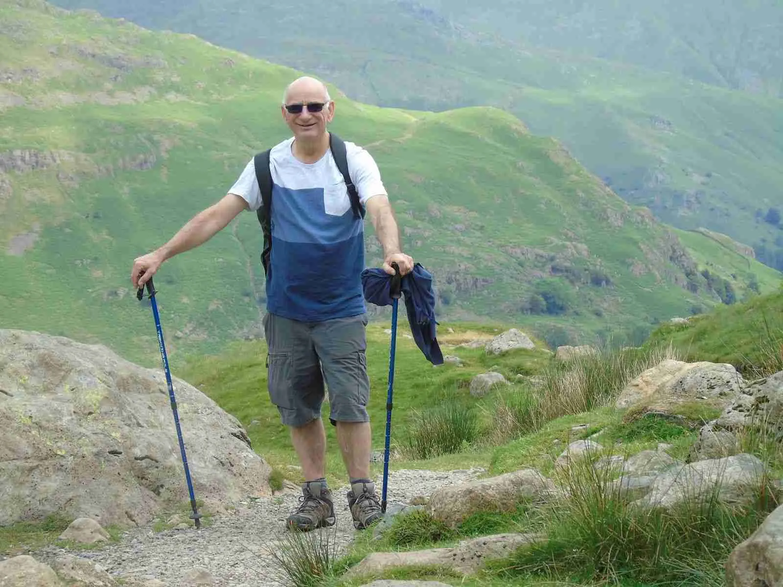 Older man hiking with trekking poles in the green Lake District mountains